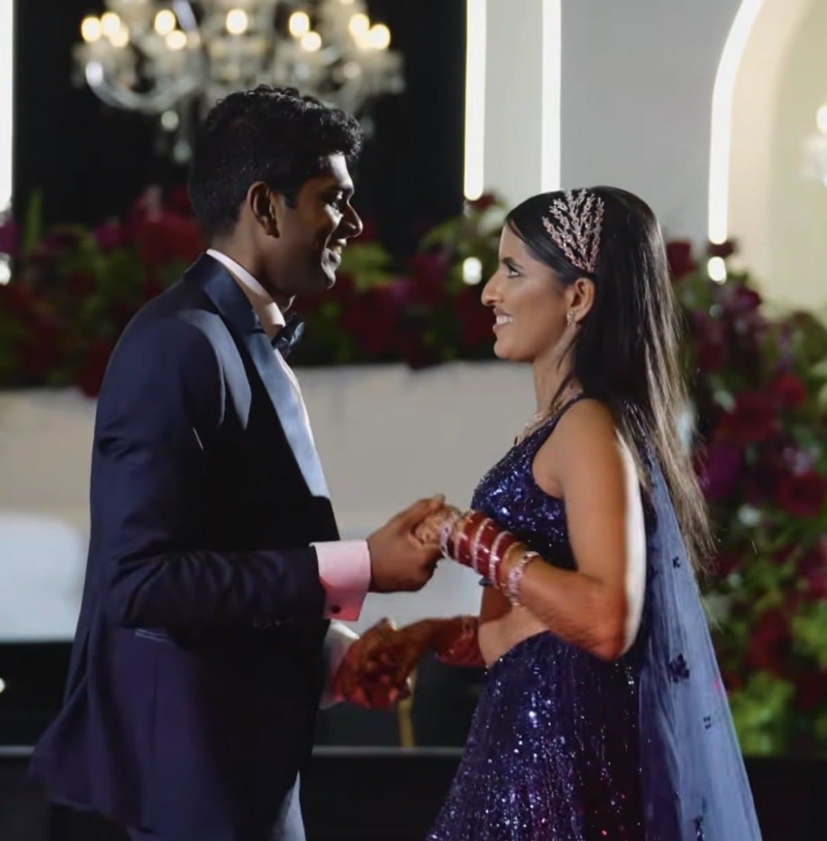 A bride and groom holding hands mid-dance in front of a wall of deep red roses