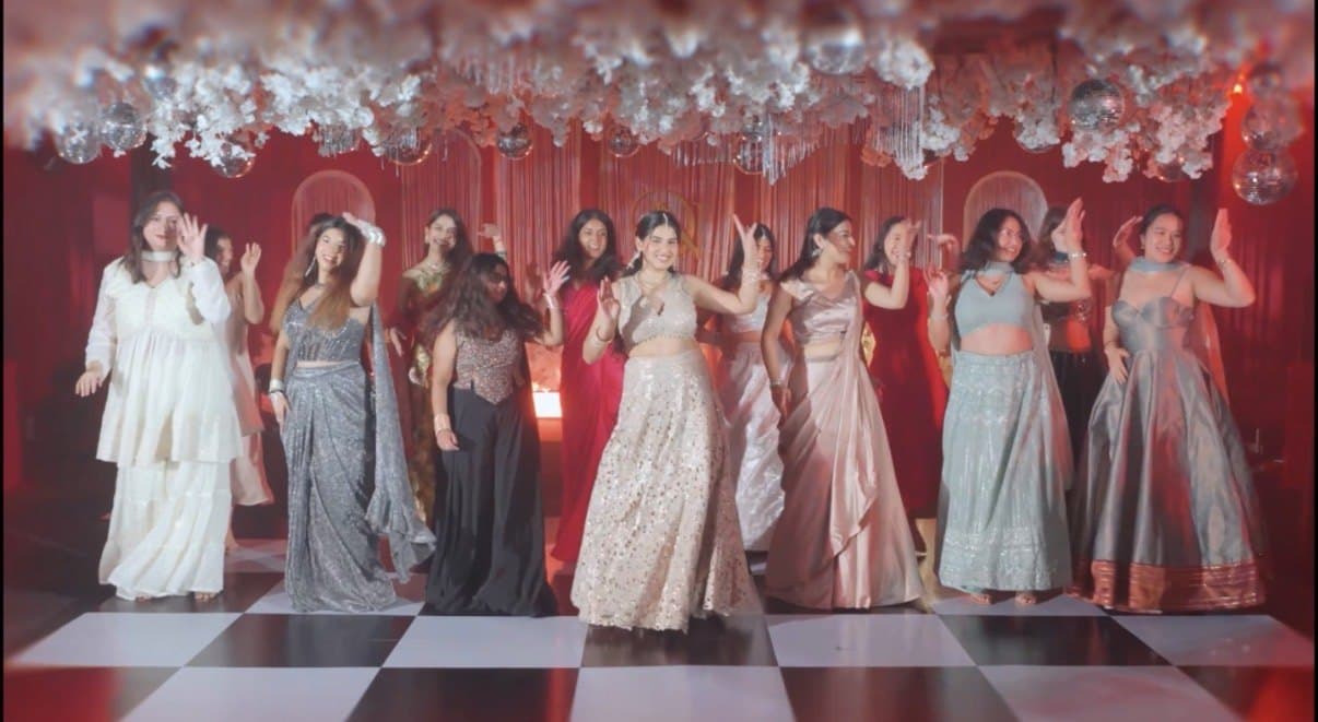 Women in pastel lehengas dancing under a white floral canopy hung with mirror balls